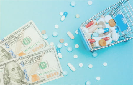 mini shopping cart with pills spilling out onto cash