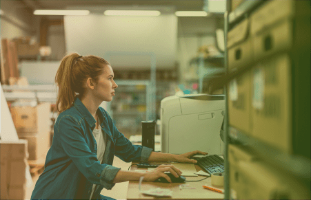 Woman sitting at desktop computer and next to printer, planning