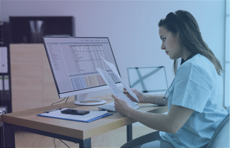 Woman with papers in her hand sitting at desk with computer monitor