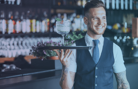 Waiter standing in front of bar with tray of drinks in hand
