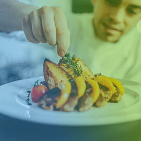 Chef plating a plate of chicken and vegetables with garnish