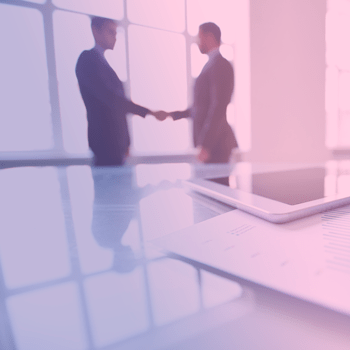 Two business professionals shaking hands with reports and a table on the table